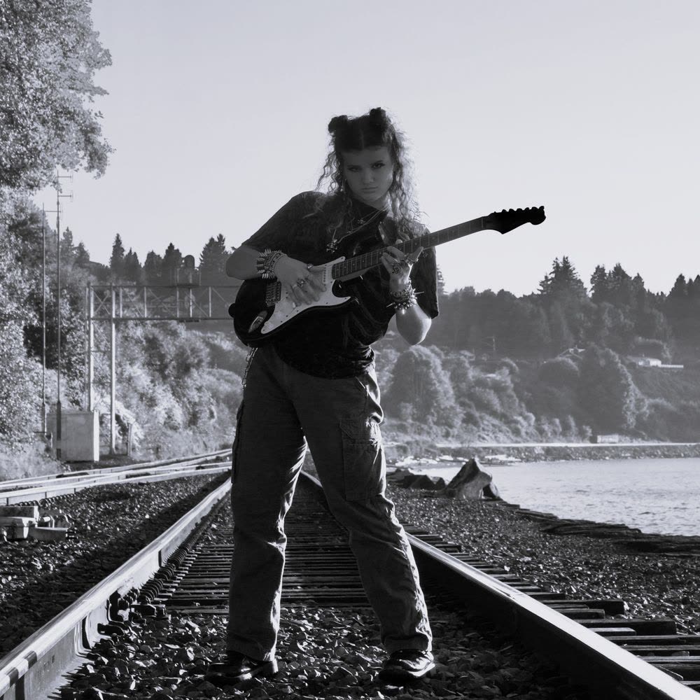 Lilla Tillo playing electric guitar on train tracks by the water