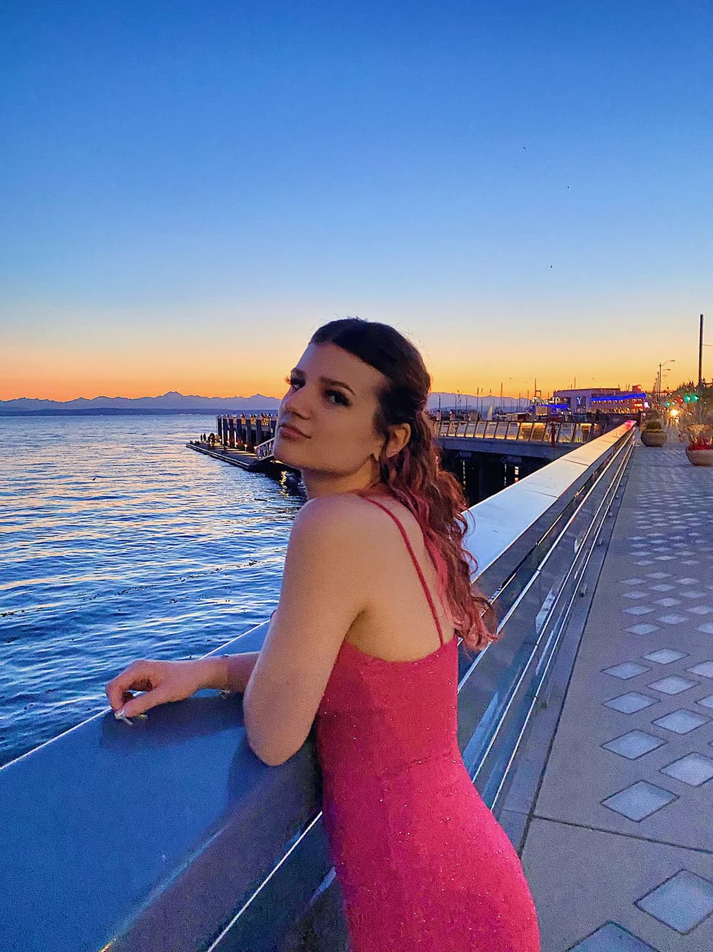 Lilla in a pink dress on a waterfront boardwalk at sunset